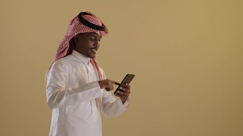 استخدام الأجهزة التقنية الحديثة، دمج التقنية والتكنولوجيا في الحياة اليومية، التواصل مع الأهل والاصدقاء، تصفح مواقع التواصل الاجتماعى، بورتريه لطالبان توأم ذو بشرة سمراء عربيان خليجيان سعوديان يرتديان الثوب والشماغ السعودي يقومان باستخدام الموبايل، خلفية بنية