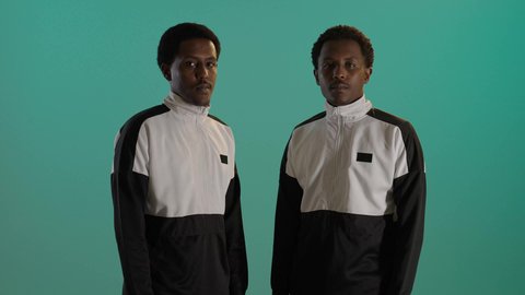 ايماءات الفرح والسعادة والنظر إلى الكاميرا، بورتريه لطالبان توأم ذو بشرة سمراء عربيان خليجيان سعوديان يرتديان اليونيفورم المدرسى، الوقوف بإستقامة بايدى متقاطعة، خلفية خضراء