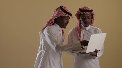 اتباع طرق تعليمية جديدة، بورتريه مقرب لطالبان توأم ذو بشرة سمراء عربيان خليجيان سعوديان يرتديان الثوب والشماغ السعودي يستخدمان اللابتوب، المذاكرة والدراسة عن بعد، المشاركة والتعاون، خلفية بنية