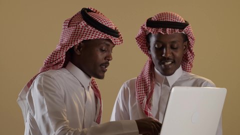 مفهوم التعليم الإلكتروني، بورتريه مقرب لطالبان توأم ذو بشرة سمراء عربيان خليجيان سعوديان يرتديان الثوب والشماغ السعودي يستخدمان اللابتوب، المذاكرة والدراسة عن بعد، المشاركة والتعاون، خلفية بنية