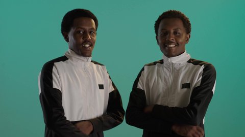 بورتريه لطالبان توأم ذو بشرة سمراء عربيان خليجيان سعوديان يرتديان اليونيفورم المدرسى، الوقوف بإستقامة بايدى متقاطعة، إيماءات وجه ويدين تدل على السعادة الثقة، خلفية خضراء