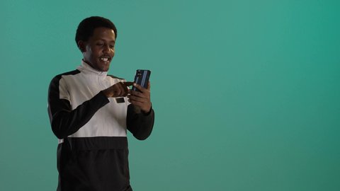 التواصل مع الأهل والاصدقاء، بورتريه لطالبان توأم ذو بشرة سمراء عربيان خليجيان سعوديان يرتديان اليونيفورم المدرسىي يقومان بتصفح الهاتف المحمول، استخدام الأجهزة التقنية الحديثة، خلفية حضراء