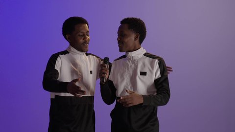 تسجيل مقطع صوتي غنائي، بورتريه لطالبان توأم عربيان خليجيان سعوديان يرتديان الزى المدرسى، تعابير الاندماج والسرور بالاستماع الى الموسيقى، خلفية ملونة