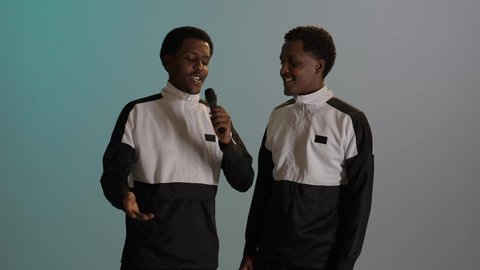 مفهوم الغناء والطرب، بورتريه لطالبان توأم ذو بشرة سمراء عربيان خليجيان يرتديان الزى المدرسى، تعابير الاندماج والسرور بالاستماع الى الموسيقى، خلفية ملونة