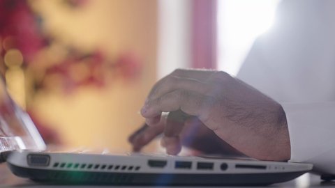 مهارة الايدي السريعة على لوحة المفاتيح، دمج التكنولوجيا مع الحياة اليومية، الاستمتاع بشرب المشروبات الساخنة، أجواء الهدوء والاسترخاء داخل كافيه راقي، تصوير مقرب لرجل خليجي عربي سعودي يرتدي الثوب التقليدي والشماغ يجلس على الكرسي يعمل على حاسب محمول وبجانبه كأس من الشاي