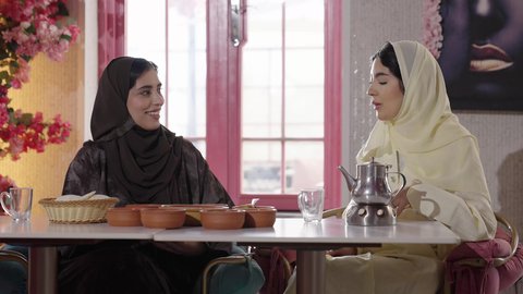 علاقات إجتماعية، صداقات و تعارف، تطوير العلاقات الإجتماعية، جلسة وناسة يوم الاجازة، تعابير السعادة والسرور بلمة الرفاق، كوفي شوب راقي في المملكة، التسامر والدردشة مع الأصدقاء، تصوير من الخلف لامرأة عربية خليجية سعودية محجبة تجلس مع صديقتها في المطعم
