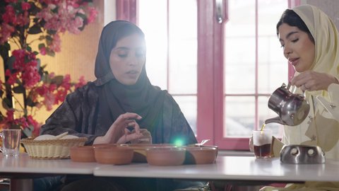 صداقات و تعارف، علاقات إجتماعية، تطوير العلاقات الإجتماعية، جلسة وناسة يوم الاجازة، تعابير السعادة والسرور بلمة الرفاق، كوفي شوب راقي في المملكة، التسامر والدردشة مع الأصدقاء، تصوير من الخلف لامرأة عربية خليجية سعودية محجبة تجلس مع صديقتها في المطعم