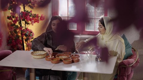 ديكور مطعم انثوي مليئ بالورود، تطوير العلاقات الإجتماعية، جلسة وناسة يوم الاجازة، تعابير السعادة والسرور بلمة الرفاق، كوفي شوب راقي في المملكة، التسامر والدردشة مع الأصدقاء، تصوير من الخلف لامرأة عربية خليجية سعودية محجبة تجلس مع صديقتها في المطعم