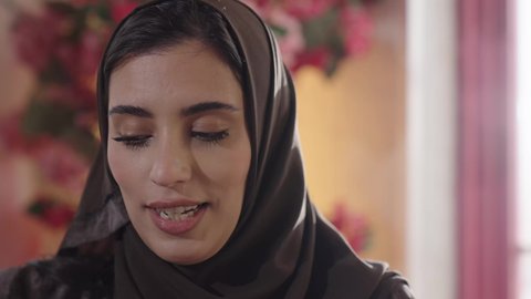 تناول الافطار في احدى المطاعم الراقية، الاستمتاع بالمشروبات الباردة, قضاء أوقات ممتعة في المطعم, مطاعم و كافيهات المملكة العربية السعودية, شابة عربية خليجية سعودية مبتسمة محجبة ترتدي العباءة والحجاب تجلس على الطاولة و تتناول الطعام