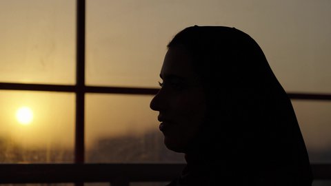 Enjoying quality time with friends, restaurants and cafes in the Kingdom, sipping your favorite drink, a close-up photograph of a veiled Saudi Arabian woman wearing an abaya, sitting in a sophisticated cafe enjoying moments of peace and relaxation, sunset photographed in the shade