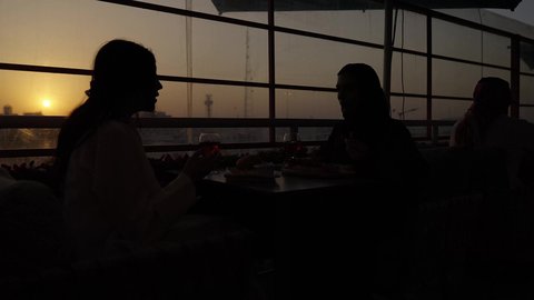 تطوير العلاقات الإجتماعية، جلسة وناسة يوم الاجازة، وقت الغروب التصوير في الظل، تعابير السعادة والسرور بلمة الرفاق، كوفي شوب راقي في المملكة، الاستمتاع بالمشروبات الباردة، التسامر والدردشة مع الأصدقاء، امرأة عربية خليجية سعودية محجبة تجلس مع صديقتها في المطعم