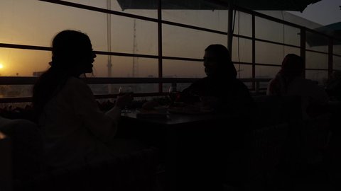 وقت الغروب التصوير في الظل، تعابير السعادة والسرور بلمة الرفاق، كوفي شوب راقي في المملكة، الاستمتاع بالمشروبات الباردة، جلسة وناسة يوم الاجازة، تطوير العلاقات الإجتماعية، التسامر والدردشة مع الأصدقاء، امرأة عربية خليجية سعودية محجبة تجلس مع صديقتها في المطعم