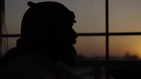 Attention to elegance and the outdoors, a sunset photoshoot, a tranquil and relaxing atmosphere inside a sophisticated cafe, a close-up of a Gulf Arab Saudi man wearing a traditional thobe and shemagh, sitting in a chair holding a glass of fresh orange juice, spending enjoyable time on the weekend.