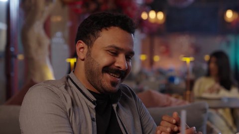 المناقشة والهزار بين الاصحاب، قضاء أوقات ممتعة مع الاصحاب، أجواء الهدوء والاسترخاء داخل كافيه راقي، تصوير مقرب لرجل خليجي عربي سعودي يرتدي الزي الكاجوال يجلس على الكرسي يحمل بيده كأس من العصير، قضاء أوقات ممتعة في الويكند