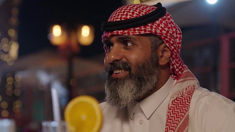 تناول الحلويات والمخبوزات، لقاء الاصدقاء في أوقات الفراغ، أجواء الهدوء والاسترخاء داخل كافيه راقي، تصوير مقرب لرجل خليجي عربي سعودي يرتدي الثوب التقليدي والشماغ يجلس على الكرسي يحمل كأس من عصير البرتقال الطبيعي، قضاء أوقات ممتعة في الويكند