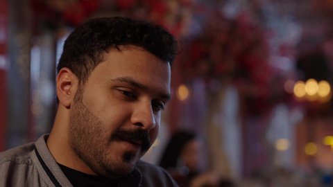 Enjoying sweets and pastries, spending quality time with friends, the peaceful and relaxing atmosphere of a sophisticated cafe, a close-up of a casually dressed Saudi Arabian Gulf man sitting in a chair holding a glass of juice, spending enjoyable times this weekend.