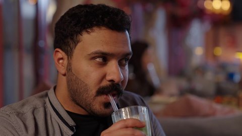 استخدام الشفاطة لشرب العصير في الكافيهات والمطاعم، قضاء أوقات ممتعة مع الاصحاب، أجواء الهدوء والاسترخاء داخل كافيه راقي، تصوير مقرب لرجل خليجي عربي سعودي يرتدي الزي الكاجوال يجلس على الكرسي يحمل بيده كأس من العصير، قضاء أوقات ممتعة في الويكند