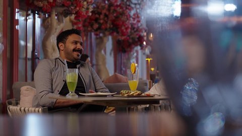 التوافق والقبول بين الاصدقاء، قضاء أوقات ممتعة في الويكند، الاستمتاع بتناول المشروبات ، تصوير مقرب لرجل عربي خليجي سعودي يرتدي الثوب و الشماغ يجلس فى المقهي برفقة صديقة، ايماءات السعادة و السرور، تناول الحلويات والمخبوزات الجاهزة كافيه راقي