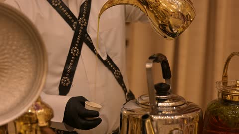 التقاليد السعودية الاصيله ، مقدم ضيافة يرتدي الزي التقليدي يقوم بسكب القهوه العربيه الاصيله من دله ذهبية اللون فى احدي قاعات الزفاف فى الدمام بالمملكة العربية السعودية، الضيافة السعودية التقليديه