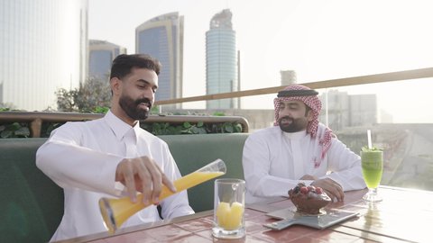 قضاء أوقات ممتعة في الويكند، الترويح عن النفسة برفقة الأصدقاء، الاستمتاع بتناول المشروبات ، تصوير مقرب لرجل عربي خليجي سعودي يرتدي الثوب و الشماغ يجلس فى المقهي برفقة صديقة، ايماءات السعادة و السرور، التسامر والضحك بين الأصدقاء، جلسة وناسة ونقاشات وحوارات