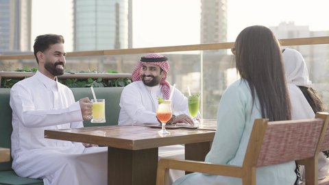 التسامر والضحك بين الأصدقاء، جلسة وناسة ونقاشات وحوارات، الترويح عن النفسة برفقة الأصدقاء، الاستمتاع بتناول المشروبات ، تصوير مقرب لرجل عربي خليجي سعودي يرتدي الثوب و الشماغ يجلس فى المقهي برفقة أصدقائه، ايماءات السعادة و السرور