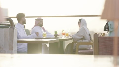 وصول احدى الصديقات التحية والسلام، التسامر والضحك بين الأصدقاء، جلسة وناسة ونقاشات وحوارات، الترويح عن النفسة برفقة الأصدقاء، الاستمتاع بتناول المشروبات ، تصوير مقرب لرجل عربي خليجي سعودي يرتدي الثوب و الشماغ يجلس فى المقهي برفقة أصدقائه، ايماءات السعادة و السرور