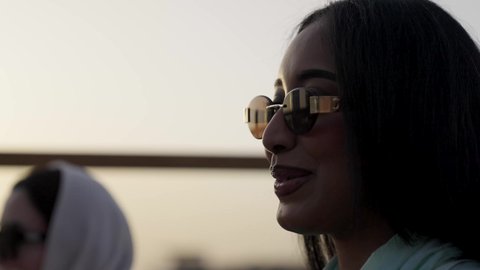 حماية العيون باستخدام النظارة الشمسية، وصول احدى الصديقات التحية والسلام، التسامر والضحك بين الأصدقاء، جلسة وناسة ونقاشات وحوارات، الترويح عن النفسة برفقة الأصدقاء، تصوير مقرب لرجل عربي خليجي سعودي يرتدي الثوب و الشماغ يجلس فى المقهي برفقة أصدقائه