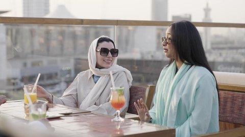 التحدث برفقه الاصدقاء، ، وصول احدى الصديقات التحية والسلام، التسامر والضحك بين الأصدقاء، جلسة وناسة ونقاشات وحوارات، الترويح عن النفسة برفقة الأصدقاء، سيدتان عربيتان خليجيتان سعوديتان تجلسان فى كافيه برفقة أصدقائهم يتبادلون الاحاديث