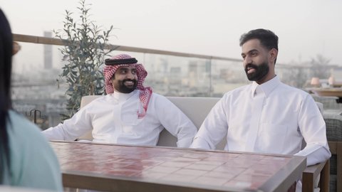 قضاء أوقات ممتعة ، التنزه في وقت العطلة ، وصول احدى الصديقات التحية والسلام، التسامر والضحك بين الأصدقاء، جلسة وناسة ونقاشات وحوارات، الترويح عن النفسة برفقة الأصدقاء، تصوير مقرب لرجل عربي خليجي سعودي يرتدي الثوب و الشماغ يجلس فى المقهي برفقة أصدقائه