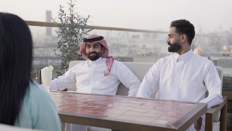 تعابير السعادة والسرور بلمة الرفاق، ، وصول احدى الصديقات التحية والسلام، التسامر والضحك بين الأصدقاء، جلسة وناسة ونقاشات وحوارات، الترويح عن النفسة برفقة الأصدقاء، تصوير مقرب لرجل عربي خليجي سعودي يرتدي الثوب و الشماغ يجلس فى المقهي برفقة أصدقائه