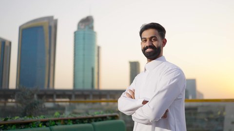 Gestures of confidence and pride, pride and honor in the Saudi state, the towers and skyscrapers of the financial economy in Riyadh at sunset, the growth and urban development in the Kingdom of Saudi Arabia, a shot from behind of a Saudi Arabian Gulf man wearing the traditional white thobe.