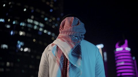 الفن الهندسي للمباني وناطحات السحاب، ، الفخر والاعتزاز بالدولة السعودية، الأبراج وناطحات السحاب المالية الإقتصادية في الرياض المضيئة في الليل، النمو والتطور العمراني في المملكة العربية السعودية، تصوير من الخلف لرجل عربي خليجي سعودي يرتديالشماغ والثوب التقليدي