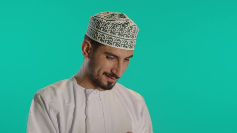 تتبع خطوات العمل باستخدام التابلت، الالعاب الالكترونية على الاجهزة الحديثة، انجاز مهام العمل عن بعد، الدردشة والتواصل مع الاصدقاء، اجراء مكالمة الفيديو باستخدام جهاز تقني حديث، رجل عربي خليجي عماني مبتسم يرتدي الكمة والدشداشة يستخدم جهاز التابلت، خلفية زرقاء