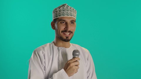 مفهوم الفن والموهبة، تبادل الحوار والاستفادة من خبرات،  إلقاء المحاضرات وإقامة الندوات، الدورات التدريبية و ورشات العمل,  بورتريه مقرب لرجل عربي خليجي عماني يرتدي الدشداشة والكمه  يحمل مكبر الصوت و ورقة بيده ويقوم بالنقاشات الهامة، خلفية زرقاء