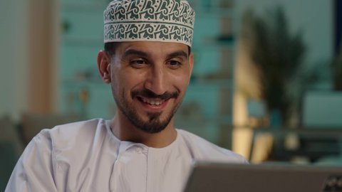 انجاز مهام العمل عن بعد، الدردشة والتواصل مع الاصدقاء، تصفح الانترنت ومواقع التواصل الاجتماعي، اجراء مكالمة الفيديو باستخدام جهاز تقني حديث، رجل عربي خليجي عماني مبتسم يرتدي الكمة والدشداشة يستخدم جهاز التابلت، مفهوم ممارسه الانشطه والعمل عن بعد