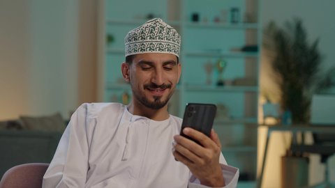 التواصل مع الأهل والأصدقاء، استخدام التكنولوجيا و التقنيات الحديثة,  البحث عن موقع شيء ما، مشاهدة الأفلام والمسلسلات الممتعة، متابعة مواقع التواصل الاجتماعي عبر الهاتف المحمول، تصوير لرجل عربي خليجي عماني يرتدي الدشداشة والكمه يحمل بيده جهاز الجوال