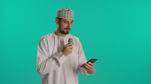 إلقاء المحاضرات وإقامة الندوات، الدورات التدريبية و ورشات العمل, تبادل الحوار والاستفادة من خبرات، بورتريه مقرب لرجل عربي خليجي عماني يرتدي الدشداشة والكمه  يحمل مكبر الصوت  وهاتف محمول بيده ويقوم بالنقاشات الهامة، إقامة الندوات وإلقاء المحاضرات، خلفية زرقاء