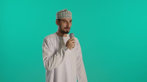 الدورات التدريبية و ورشات العمل, إلقاء المحاضرات وإقامة الندوات، تبادل الحوار والاستفادة من خبرات، بورتريه مقرب لرجل عربي خليجي عماني يرتدي الدشداشة والكمه  يحمل مكبر الصوت بيده ويقوم بالنقاشات الهامة، إقامة الندوات وإلقاء المحاضرات، خلفية زرقاء