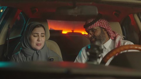 النقاش حول فكره، قضاء وقت عائلى ممتع ، زوجين سعوديين خليجيين عربيين يجلسان  داخل السيارة يقومان باستخدام الهاتف المحمول، قضاء وقت ممتع فى الخارج