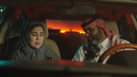 الحوار وتبادل وجهة النظر، قضاء وقت عائلى ممتع ، زوجين سعوديين خليجيين عربيين يجلسان  داخل السيارة يقومان باستخدام الهاتف المحمول، قضاء وقت ممتع فى الخارج