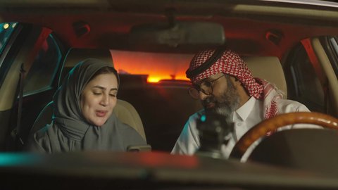 الحوار وتبادل الأفكار، قضاء وقت عائلى ممتع ، زوجين سعوديين خليجيين عربيين يجلسان  داخل السيارة يقومان باستخدام الهاتف المحمول، قضاء وقت ممتع فى الخارج