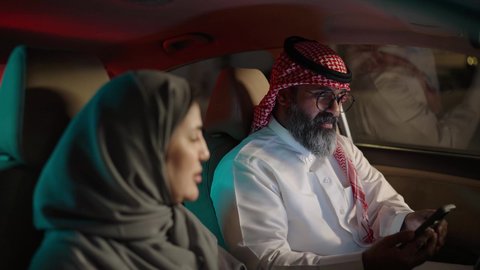 استخدام حزام الامان ، رجل عربي خليجي سعودي يرتدي الثوب الابيض و الشماغ يجلس فى السيارة برفقة زوجته ، تصفح الانترنت عبر الهاتف المحمول ، قضاء وقت ممتع فى الخارج