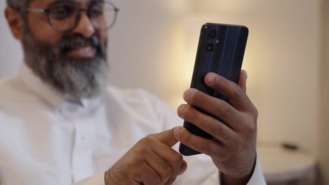 استخدام التكنولوجيا والجهاز التقني الحديث المتطور، ايماءات السعادة والفرح، تصوير مقرب لرجل عربي  خليجي سعودي مبتسم يرتدي الثوب التقليدي يمسك بيده الهاتف المحمول