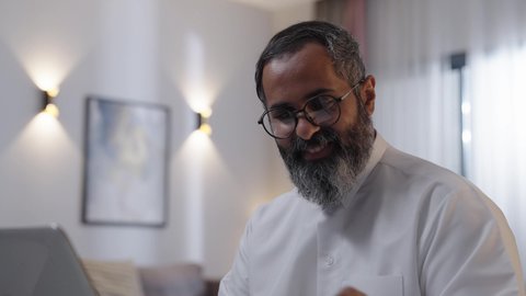 Enjoying a warm drink, typing on the keyboard, an Arab Gulf Saudi man wearing a white thobe using a laptop, the concept of remote work.