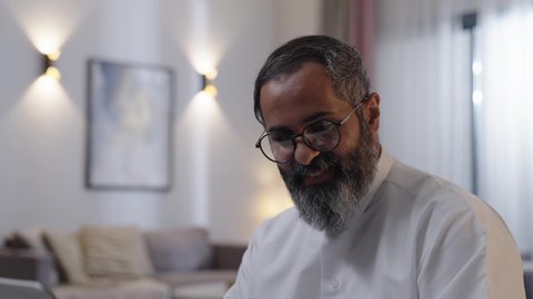 الاستمتاع بتناول المشورب المفضل ، النقر على لوحة المفاتيح ،  رجل عربي خليجي سعودي يرتدي الثوب الابيض يستخدم الحاسب المحمول، مفهوم العمل عن بعد