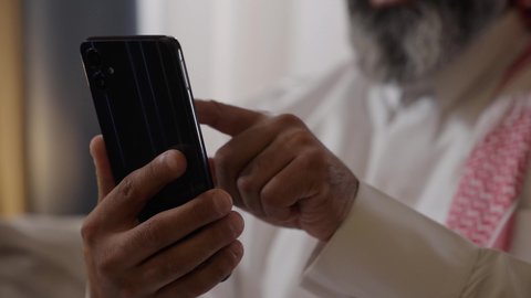 استخدام الأجهزة والتقنيات الحديثة، الدردشة والتواصل مع الاصدقاء ، تصوير مقرب ليد رجل عربي خليجي سعودي يمسك بيده الهاتف المحمول يقوم بتصفح الانترنت ومواقع التواصل الاجتماعي