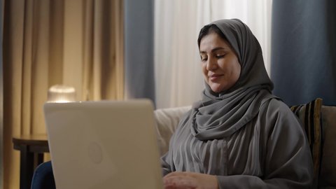 التعاون وتبادل الآراء والمشاركة بين الزوجين، ادارة الأعمال عن بعد، استخدام الأجهزة والتقنيات الحديثة والمتطورة،امراه عربيه خليجيه محجبة ترتدي العباءة تقوم باستخدام الحاسوب المحمول بجانب زوجها، إنجاز المهام في المنزل