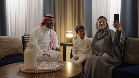 فرحة الأبناء بقضاء وقت ممتع مع الأهل، التقاط سيلفي عائلي تذكاري عبر الهاتف المحمول, عائلة عربية سعودية خليجية مبتسمة تقوم بتوثيق اللحظات الممتعة بإيماءات السعادة والفرح, الاجتماع الأسري في غرفة المعيشة وبناء مجتمع سعودي متنامي