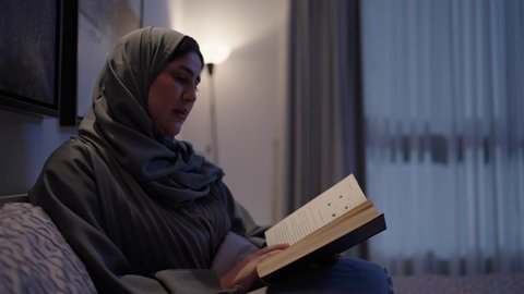 مفهوم التثقيف والبحث العلمي، اتباع أسلوب حياة صحي، قراءة الروايات والقصص الممتعة، الاسترخاء والاستمتاع بالأجواء الهادئة، الشعور بالراحة والطمأنينة، سيدة عربية خليجية سعودية تجلس في سرير مريح تمسك بيدها الكتاب