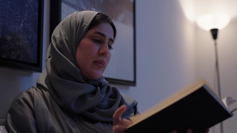 الشعور بالراحة والطمأنينة، الاسترخاء والاستمتاع بالأجواء الهادئة, قراءة الروايات والقصص الممتعة، سيدة عربية خليجية سعودية تجلس في سرير مريح تمسك بيدها الكتاب، اتباع أسلوب حياة صحي